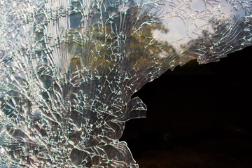 Broken window with cracks all over. Some reflection of tree and sky visible
