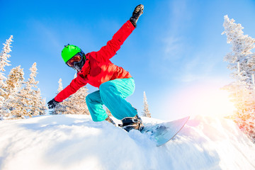 Active man snowboarder riding on slope during sunny day in mountains. Dust snow forest