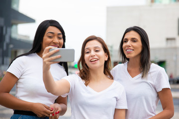 Joyful women posing for selfie on street. Cheerful young ladies taking selfie with smartphone. Concept of self portrait