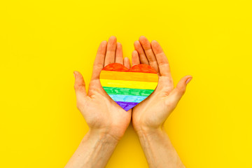 LGBT symbol. Rainbow heart in hands on yellow background top-down