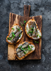Grilled bread sardines micro greens sandwiches on a rustic cutting board on a dark background, top...