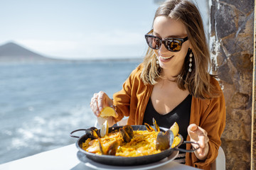 Woman eating paella, traditional spanish dish, while sitting at the restaurant terrace near the...