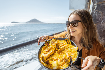 Woman eating paella, traditional spanish dish, while sitting at the restaurant terrace near the...
