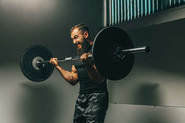 Fototapeta na wymiar Muscular man in black sportswear lifting barbell in a gym