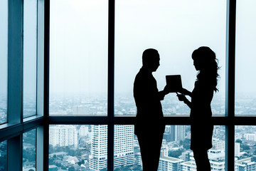 Silhouette of two office workers discussing work by the window