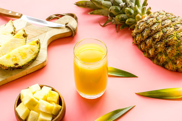 Pineapple juice in glass closeup near sliced fruit on pink background