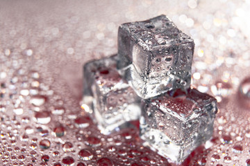 Melting ice cubes on red background with a drops of water