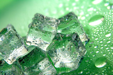 Melting ice cubes on a green background with a drops of water