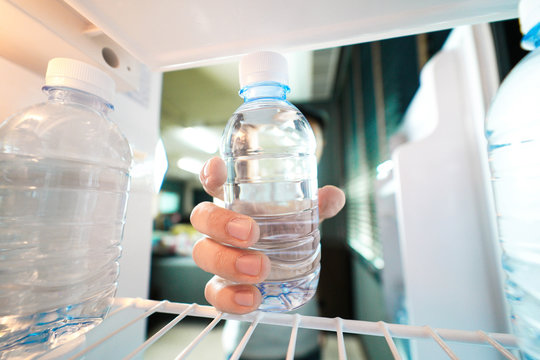 Hand reaching into refrigerator taking a plastic bottle of water out. Wide angle perspective.