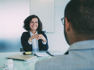 Personnel manager interviewing male candidate. Business man and happy woman sitting at meeting table opposite of each other. Job meeting concept