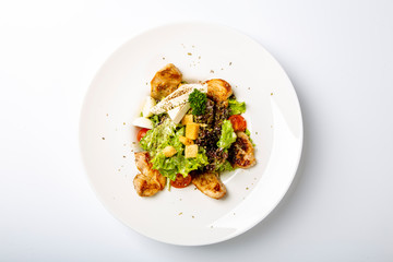 Caesar with chicken and feta cheese.  Served on a round white plate: pieces of fried chicken, cheese, tomatoes, salad. Plate on a white background. 