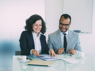 Satisfied business partners closing agreement. Happy business man and woman sitting at meeting table and picking documents. Contract or paperwork concept