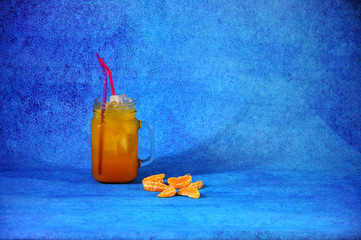 Glass mug of citrus juice with ice and slices of mandarin on a blue background. © Алексей Желтухин