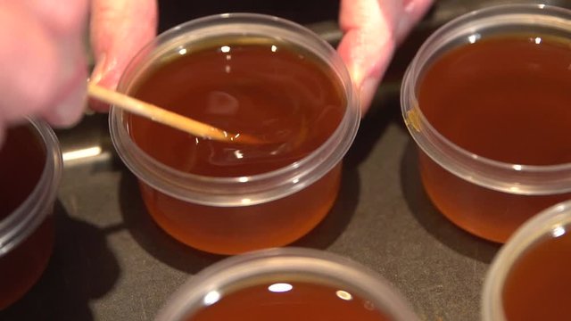 Woman pouring essential oil from glass bottle into bowl on table