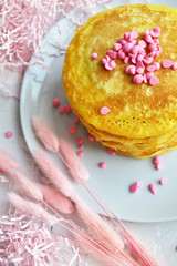 pancakes with pink topping on a white plate next to pink fluffy grass on a blue table