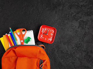 Orange backpack with school supplies on a black concrete background. The concept of the school.