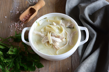 Meat soup with noodles in a white plate on a gray napkin