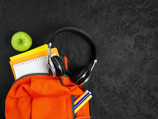 Orange backpack with school supplies on a black concrete background. The concept of the school.