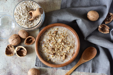 Milk oatmeal porridge with nuts, dried apricots and honey in a wooden plate close-up on a gray background