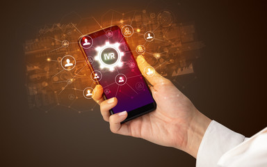 Female hand holding smartphone with IVR abbreviation, modern technology concept