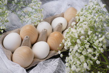 Happy Easter. White chicken eggs, wooden eggs in a stand on a wooden background with white gypsophila flowers. The concept of holidays. Trend.