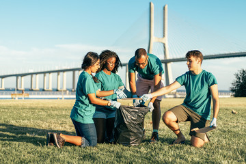 Multiethnic volunteer team removing garbage from grass into plastic bag. Men and women wearing uniforms picking up rubbish from lawn. Trash removal concept