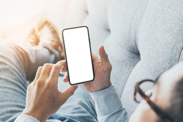Mockup image blank white screen cell phone.man hand holding texting using mobile on sofa at home.background empty space for advertise text.people contact marketing business,technology