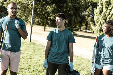 Volunteer team collecting rubbish outdoors and having fun. Young woman and men standing on grass,...