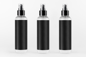 Tall transparent spray dispenser bottles for cosmetics product collection with black label in a row on white background, mock up for design.