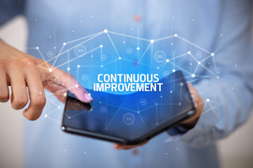 Businessman holding a foldable smartphone with CONTINUOUS IMPROVEMENT inscription, new technology concept