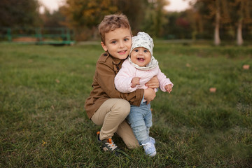 Fototapeta premium A little boy dressed in a brown coat smile and hug a his sister