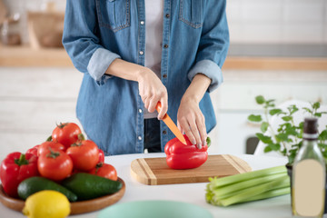 Female hands holding a knife and red pepper.