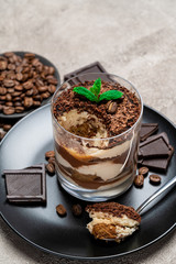 Classic tiramisu dessert in a glass cup, pieces of chocolate on concrete background