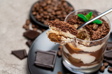 Classic tiramisu dessert in a glass cup, pieces of chocolate on concrete background