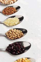 spoons with different cereals are laid out in an even row on the table. orange, black and white cereals