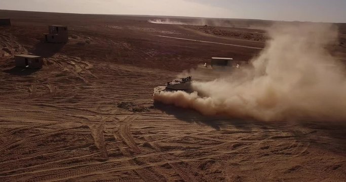 Military tank driving threw the desert leaving trail of smoke and dust