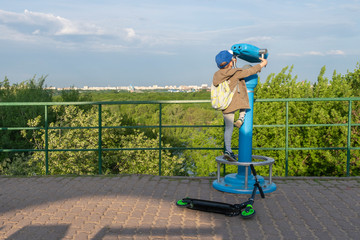 Observation deck. Boy paused his scooter trip to enjoy panoramic view with blue binoculars in...