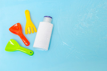 Sunscreen cream spf lotion to remedy kids skin from sun with colorful water toys on blue water surface of pool, top view. Concept ultraviolet protection product, summer children cosmetics.