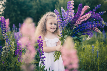 Cute baby in a white dress holds a large bouquet of flowers in nature