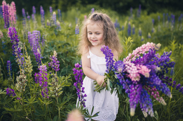 Fototapeta premium Cute baby in a white dress holds a large bouquet of flowers in nature