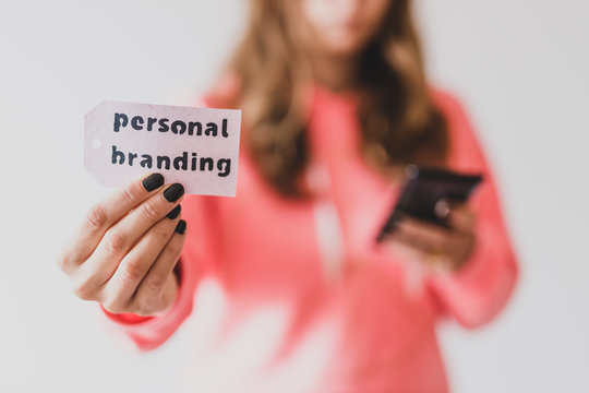 influencers and fame, girl holding Personal Branding message on price tag close to the camera and holding her phone in the other hand shot at shallow depth of field