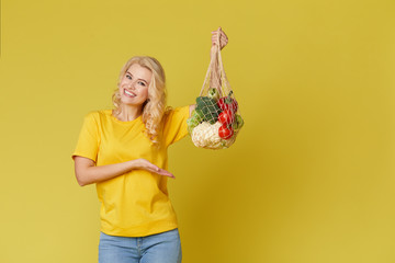 Young woman hold a string bag full of organic vegetables on yellow background. Zero waste concept. Emty space for text. Healthy Eating, Vegetarianism