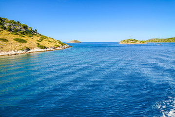 Obraz premium Adriatic coast with rocky beach, small islands, boats and sailing yachts in the blue sea, Croatia, Dalmatia