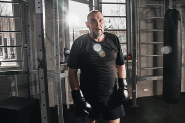 Adult gray-haired male boxer at workout in gym, boxing with gloves. The concept of a healthy lifestyle in old age