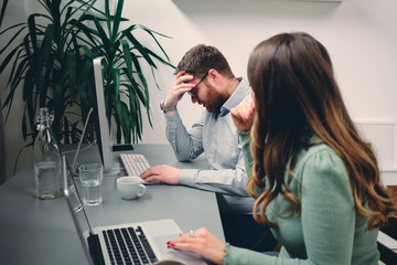 Young male having headache at work. His colleague trying to help.	