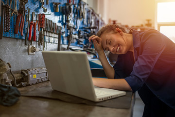 Mechanic using laptop at the repair garage. Young female mechanic with laptop. Business woman at a factory. Mechanic typing on a laptop at the repair garage