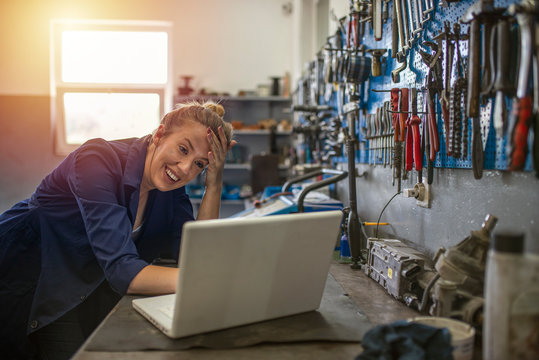 Portrait of a young female mechanic using a laptop. Female mechanic using laptop in a workshop. Business woman at a factory. Craftswoman working using a laptop in the garage.