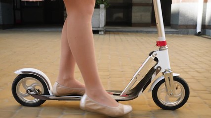 Closeup 4k video of camera following female feet in ballet flats standing and riding on scooter on the city street