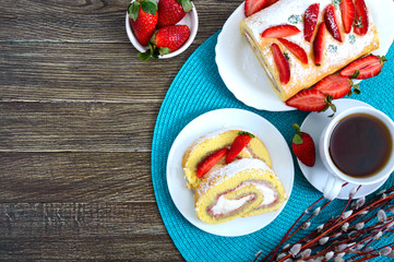 Sweet biscuit roll with strawberries and cream fresh berries and tea on a wooden background. The top view