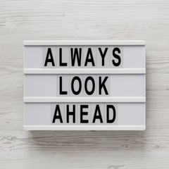 'Always look ahead' words on a modern board, clipboard with blank sheet of paper on a white wooden background, top view. Overhead, from above, flat lay.